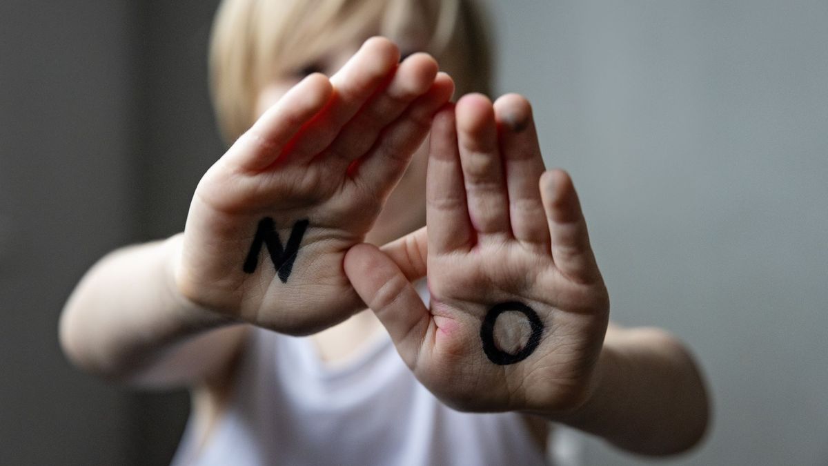 Kid with open hand palms showing word no written on them